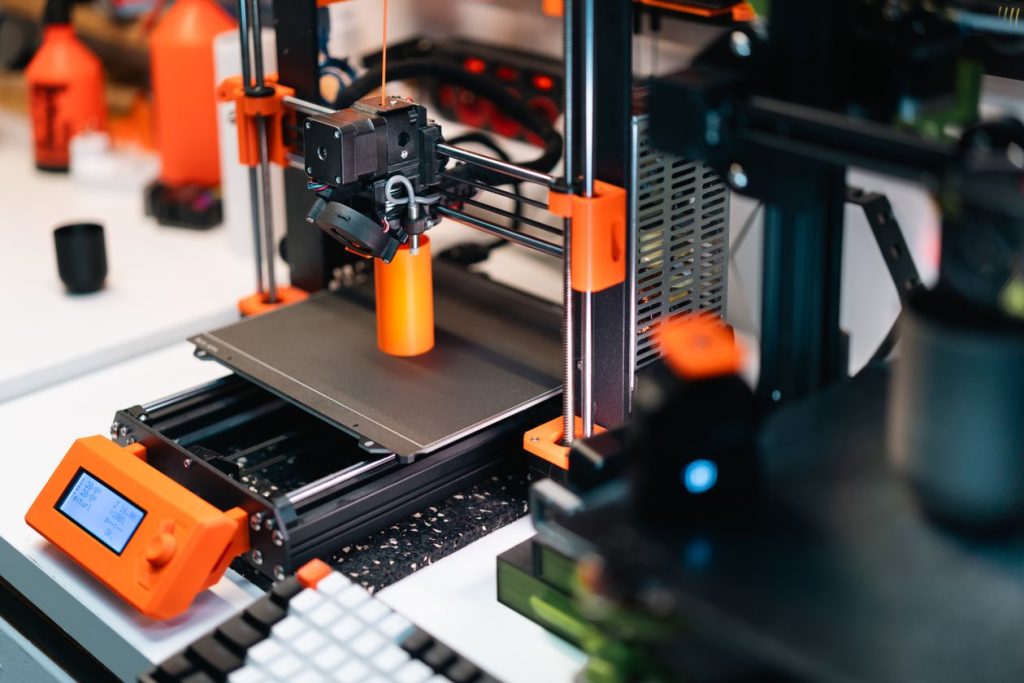 Drukarka 3D drukująca prototyp z pomarańczowymi elementami